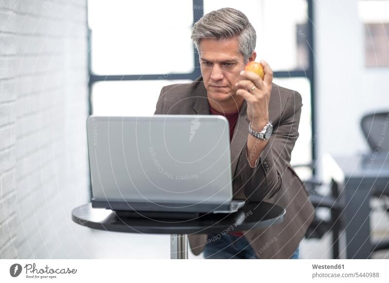 Businessman lookking at laptop, holding apple Business man Businessmen Business men using laptop using a laptop Using Laptops working At Work Success successful