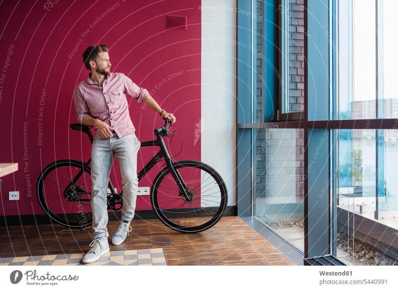 Man with bicycle standing in modern office looking out of window bikes bicycles man men males Adults grown-ups grownups adult people persons human being humans