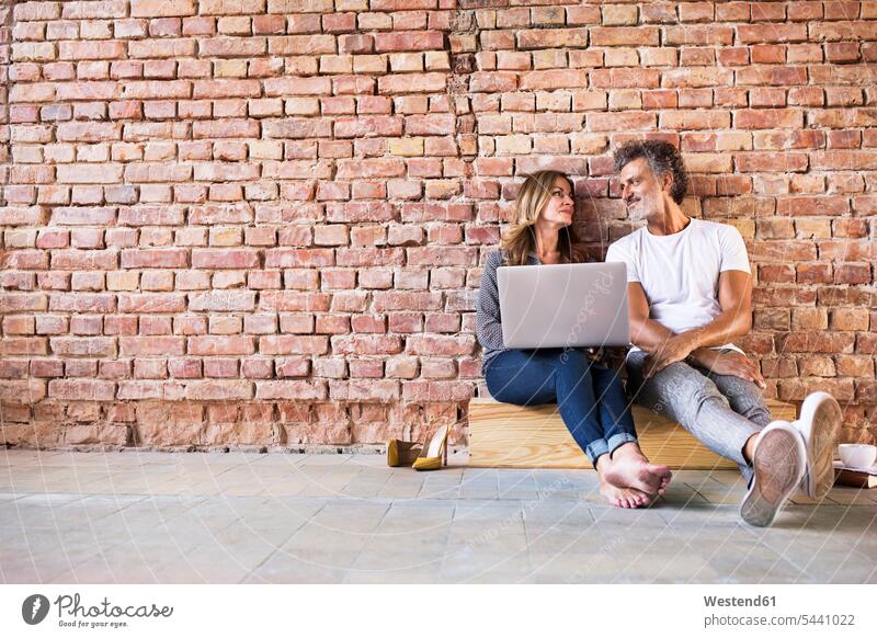 Businessman and woman sitting in a loft, using laptop, founding a start-up company business people businesspeople company foundation setting up business