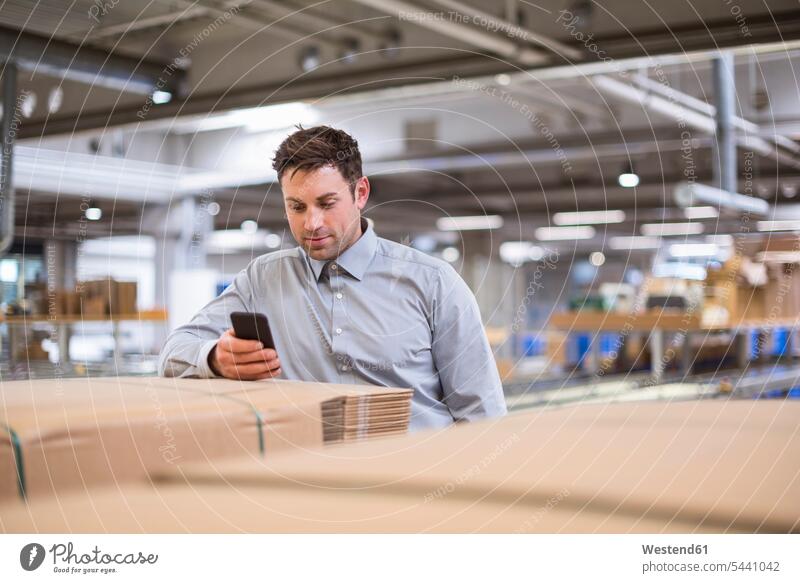Man in factory looking at cell phone mobile phone mobiles mobile phones Cellphone cell phones storehouse storage warehouse man men males Businessman