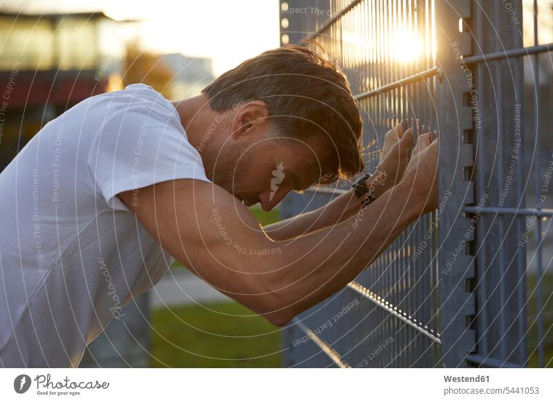 Exhausted athlete leaning against fence Sportspeople Sportsman Sportsperson athletes Sportsmen city town cities towns urban urbanity Jogging males sport sports
