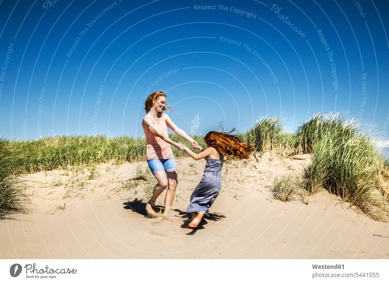 Netherlands, Zandvoort, happy mother and daughter dancing in beach dunes Fun having fun funny family families happiness daughters smiling smile sand dune