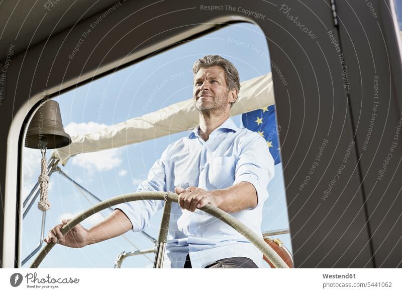 Mature man at helm of his sailing boat men males navigating navigate Adults grown-ups grownups adult people persons human being humans human beings boats