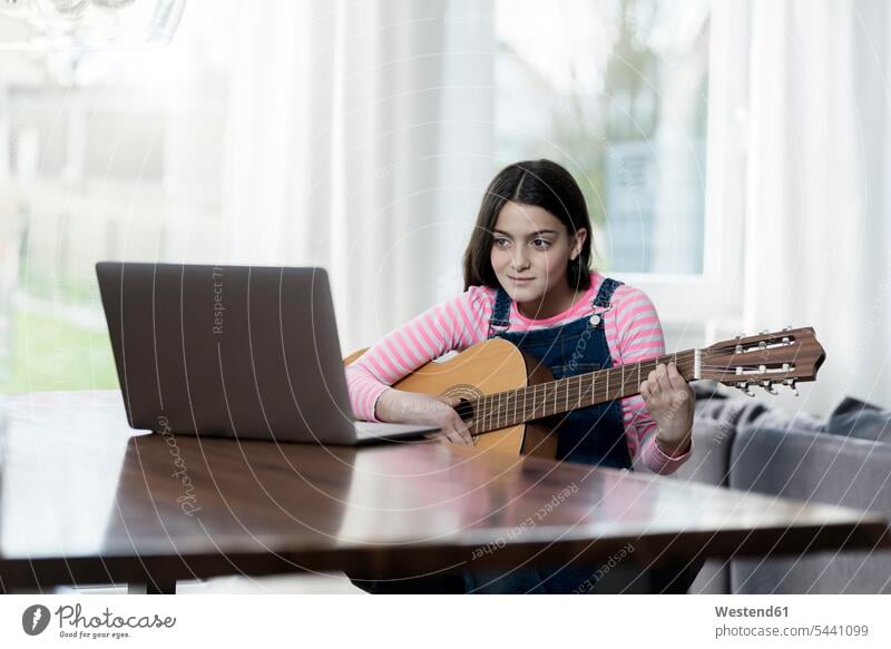 Girl playing guitar in front of laptop girl females girls Laptop Computers laptops notebook sitting Seated guitars child children kid kids people persons