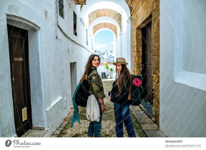 Spain, Andalusia, Vejer de la Frontera, two young women walking in the alley El Callejon de las Monjas lane Laneway female friends smiling smile path trail