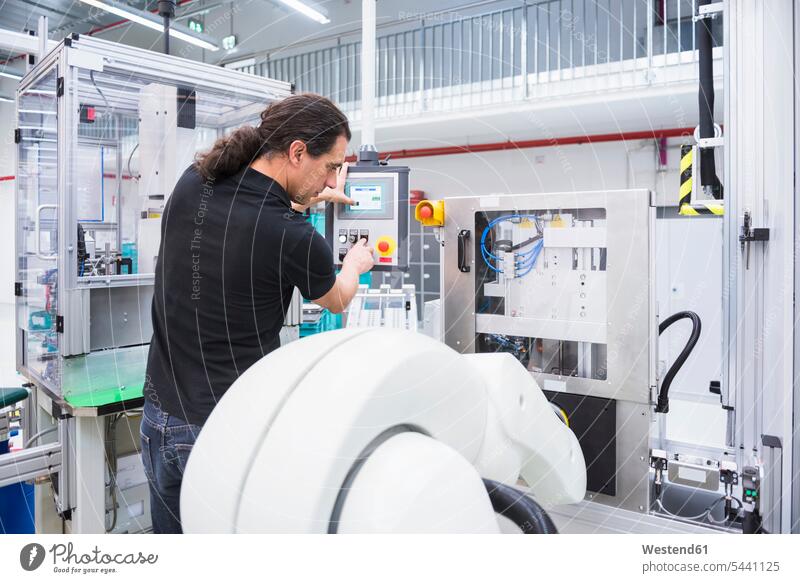 Man operating assembly robot in factory working At Work man men males Robot factories Adults grown-ups grownups adult people persons human being humans