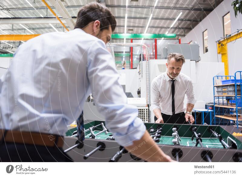 Two colleagues playing foosball in factory factories Businessman Business man Businessmen Business men smiling smile business people businesspeople