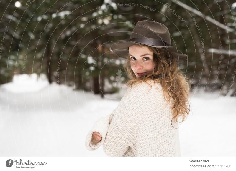 Portrait of smiling young woman wearing hat and knit pullover in winter forest portrait portraits females women Adults grown-ups grownups adult people persons
