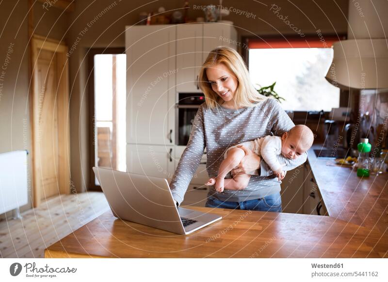 Smiling mother with baby in kitchen using laptop Laptop Computers laptops notebook infants nurselings babies mommy mothers ma mummy mama computer computers