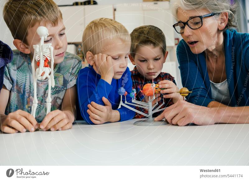 Pre-school teacher explaining solar system model to boys in kindergarten skeleton skeletons looking eyeing nursery school child children kid kids educator