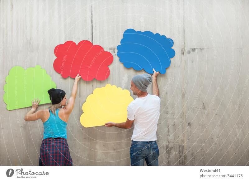 Man and woman attaching colourful cloud shapes to concrete wall multi-coloured multicoloured multi colored Multi Coloured colorful men males concrete walls