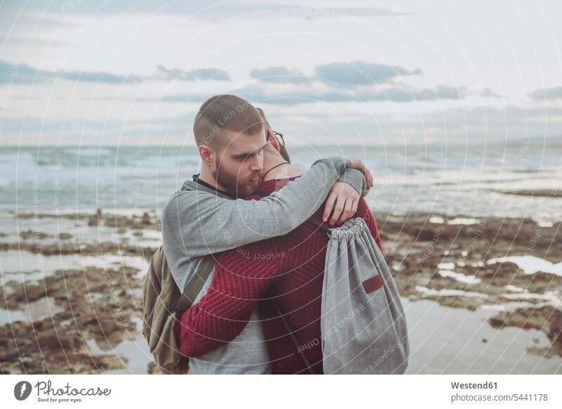 Young gay couple with backpacks hugging on the beach twosomes partnership couples beaches people persons human being humans human beings homosexual queer