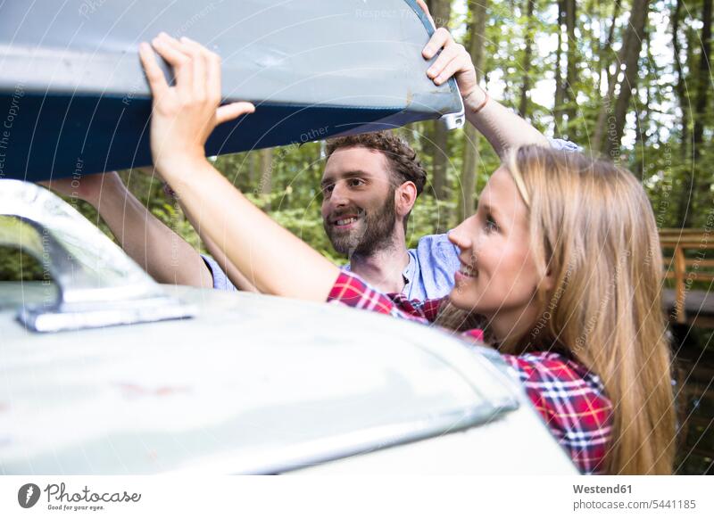 Smiling young couple taking canoe from car roof forest woods forests twosomes partnership couples take automobile Auto cars motorcars Automobiles smiling smile