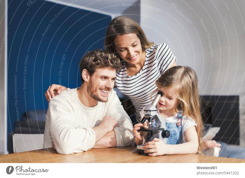 Parents watching daughter use a microscope, smiling proudly smile playing clever smart girl females girls microscopes father pa fathers daddy dads papa Pride