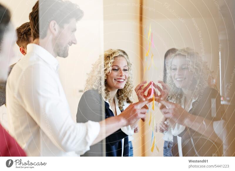 Smiling colleagues in office at glass pane with adhesive notes offices office room office rooms Business Meeting business conference meeting smiling smile