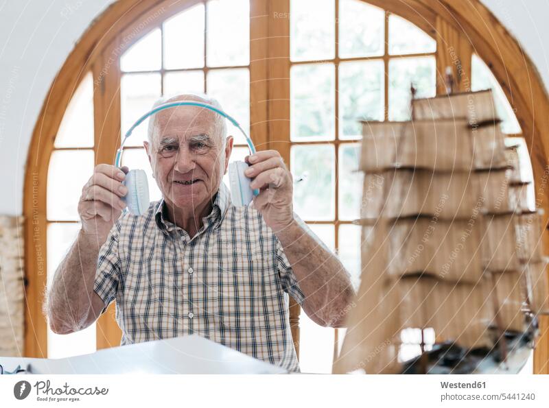 Portrait of confident senior man unpacking headphones from package with model ship on table model boat smiling smile headset senior men elder man elder men