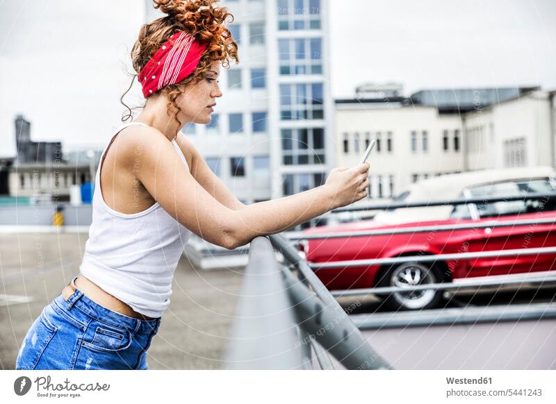Redheaded woman on parking level holding cell phone females women mobile phone mobiles mobile phones Cellphone cell phones Adults grown-ups grownups adult