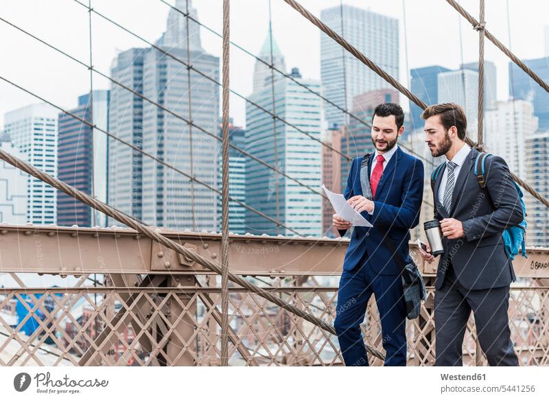 USA, New York City, two businessmen discussing document on Brooklyn Bridge talking speaking New York State bridge bridges Businessman Business man Businessmen