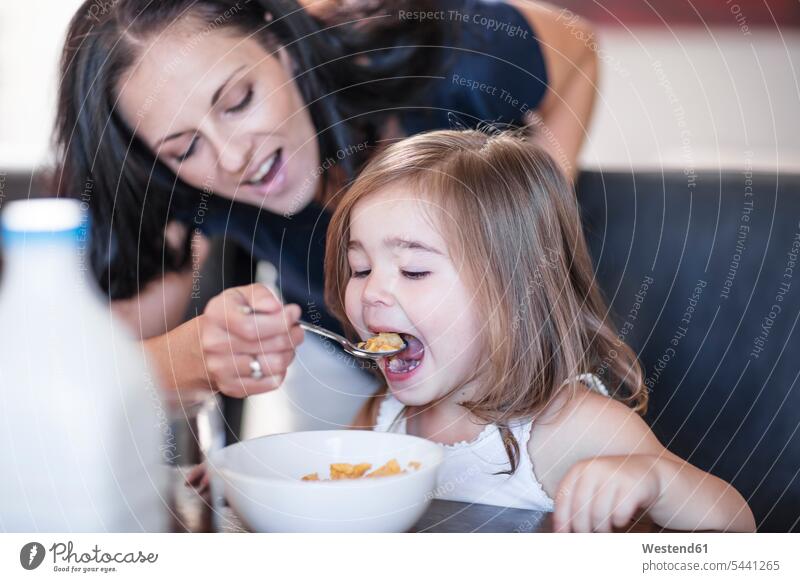 Mother feeding daughter breakfast cereal at table daughters home at home eating mother mommy mothers ma mummy mama Breakfast child children family families
