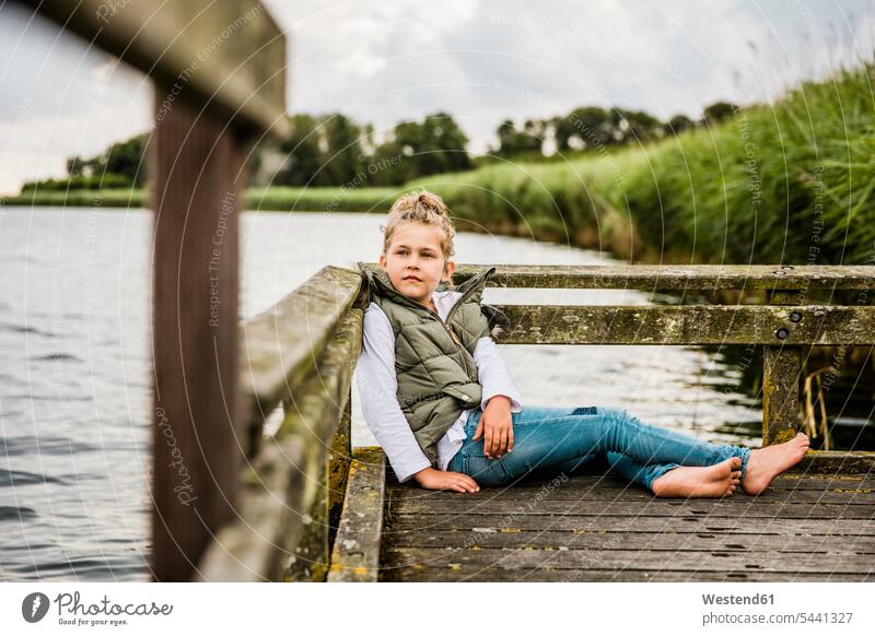 Girl sitting on jetty at a lake girl females girls Seated jetties lakes child children kid kids people persons human being humans human beings water waters