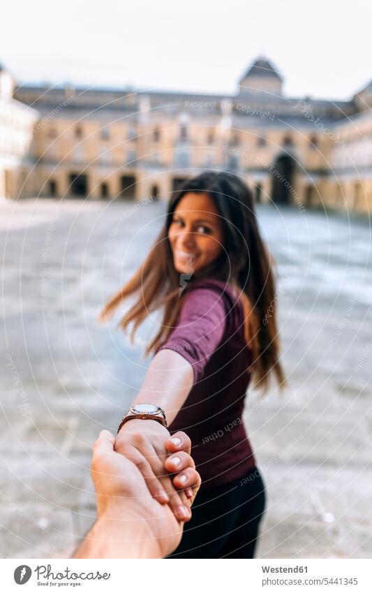 Happy young woman holding hand on urban square couple twosomes partnership couples smiling smile females women people persons human being humans human beings