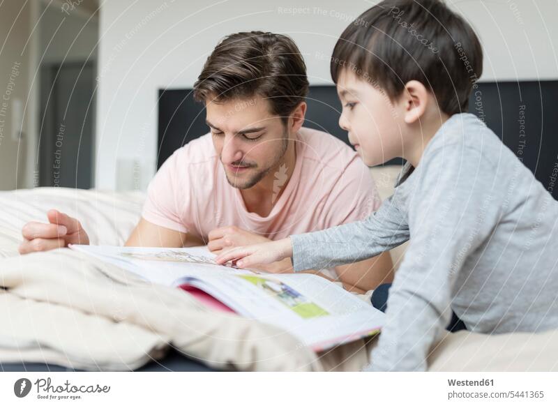 Father and son reading a book in bed beds books father pa fathers daddy dads papa sons manchild manchildren parents family families people persons human being