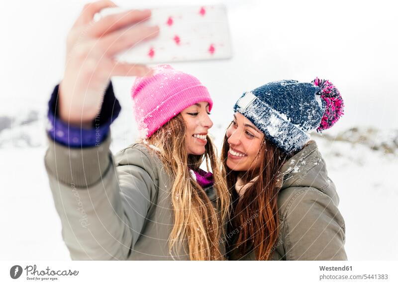 Two friends taking smart phone selfies in the snow female friends friendship winter hibernal mobile phone mobiles mobile phones Cellphone cell phone cell phones