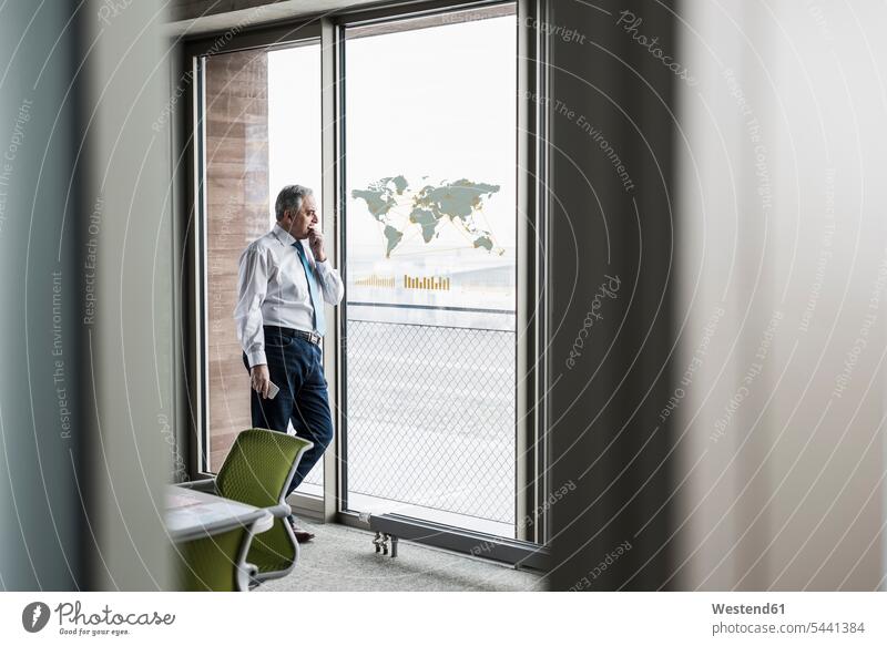 Businessman looking at windowpane with world map in office Business man Businessmen Business men world maps business people businesspeople business world
