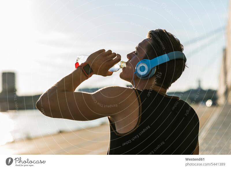 Young man wearing headphones, drinking water sportive sporting sporty athletic jogger joggers Water music men males athlete Sportspeople Sportsman Sportsperson