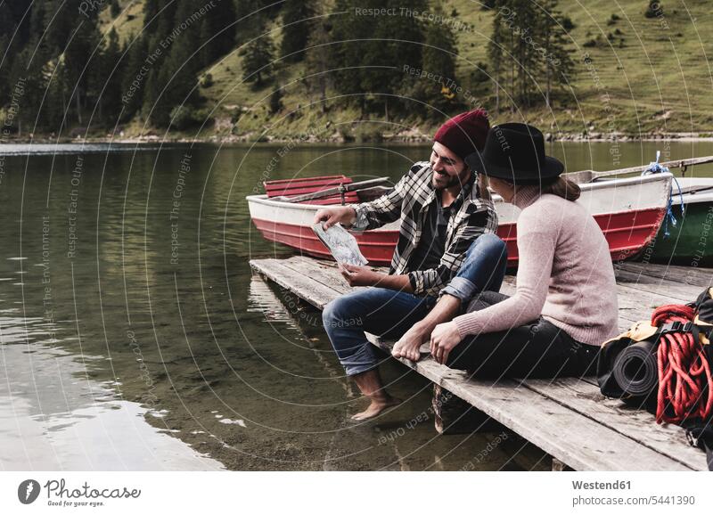 Austria, Tyrol, Alps, couple with map sitting on jetty at mountain lake lakes twosomes partnership couples smiling smile water waters body of water people