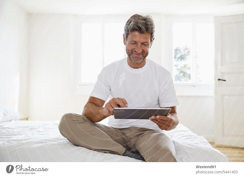 Portrait of mature man with digital tablet in bedroom Domestic Bedroom men males sitting Seated digitizer Tablet Computer Tablet PC Tablet Computers iPad