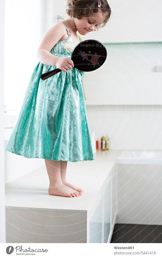 Little girl with hand mirror standing in bathroom looking at her feet females girls child children kid kids people persons human being humans human beings