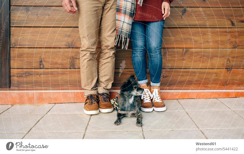 Low section of couple with dog standing in front of wooden wall dogs Canine twosomes partnership couples pets animal creatures animals people persons