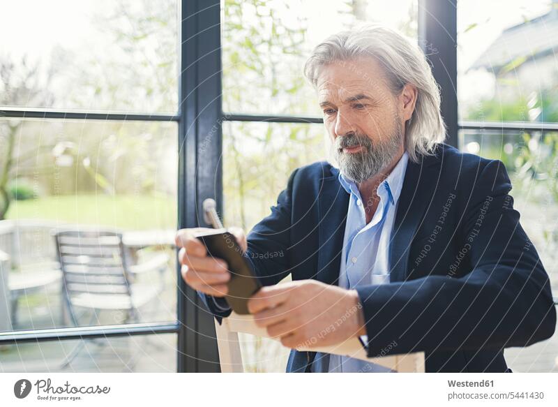 Senior businessman sitting on chair, using smartphone men males mobile phone mobiles mobile phones Cellphone cell phone cell phones reading text messaging SMS
