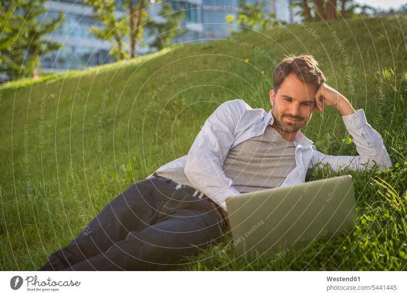 Man lying on grass using his laptop Laptop Computers laptops notebook relaxation relaxed relaxing Grassy meadow meadows man men males park parks laying down lie