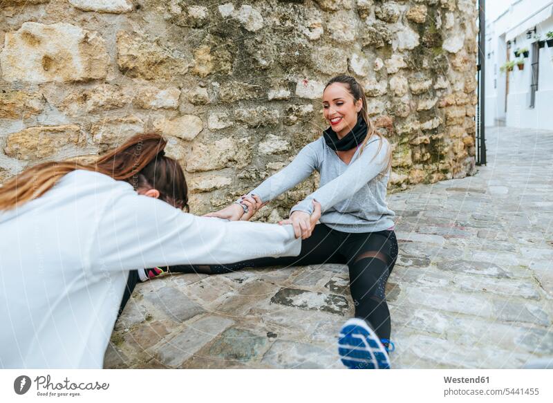Two young women dong stretching exercises in the street female friends exercising training practising together warming up warm up mate friendship sport sports