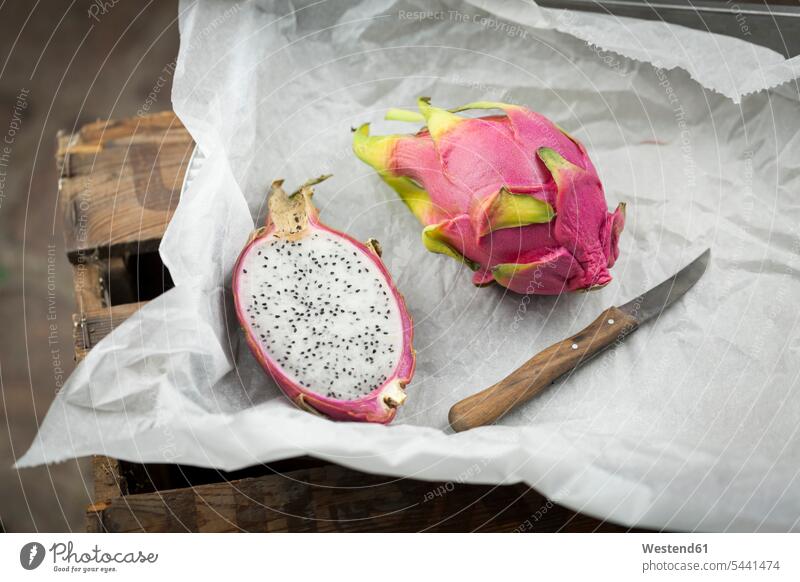 Whole and a half dragon fruit and kitchen knife on white paper food and drink Nutrition Alimentation Food and Drinks exotic Exoticism exotical outlandish opened