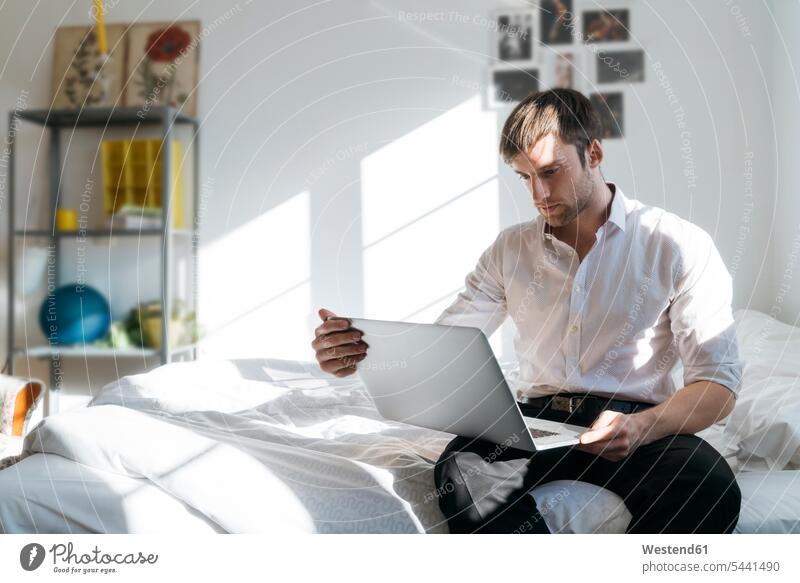 Young man sitting on bed using laptop Laptop Computers laptops notebook men males beds computer computers Adults grown-ups grownups adult people persons
