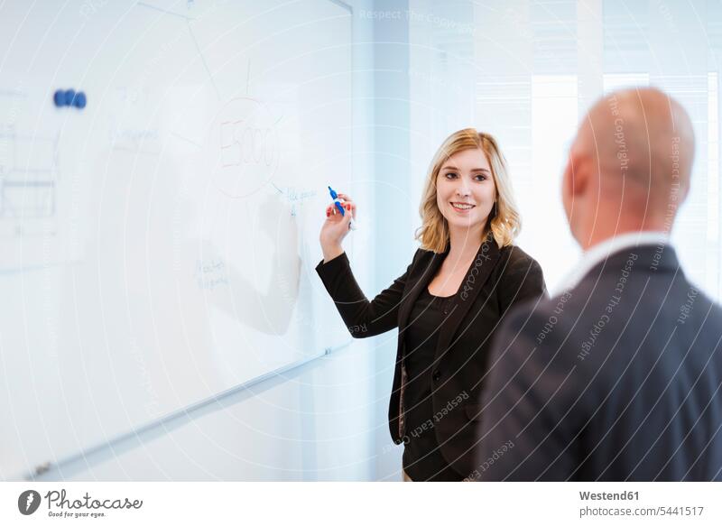 Businessman looking at businesswoman at whiteboard in office offices office room office rooms businesswomen business woman business women writing write
