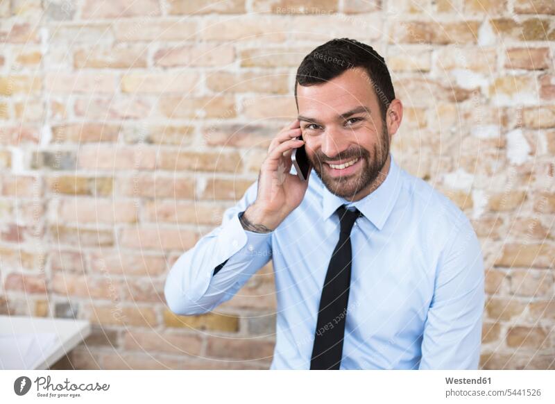 Portrait of smiling businessman on the phone at brick wall smile brick walls call telephoning On The Telephone calling mobile phone mobiles mobile phones