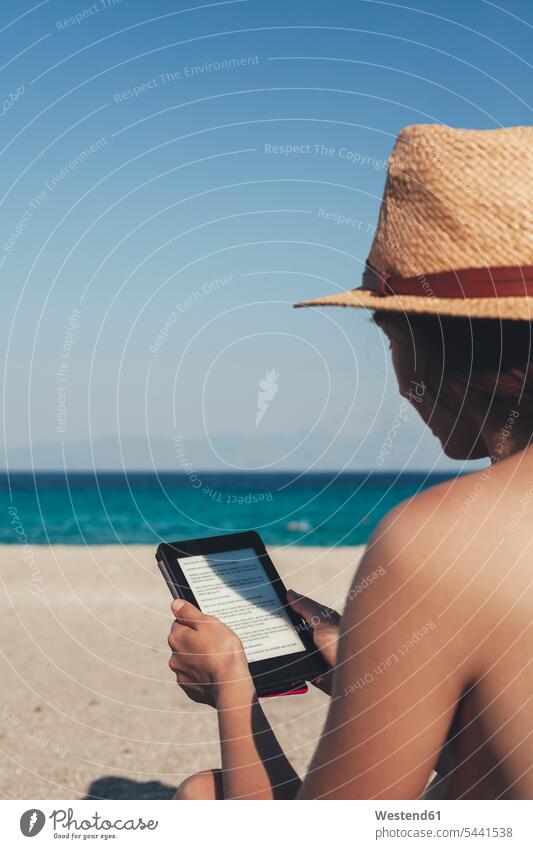 Greece, young woman on the beach reading e-book E-Book ebook electronic book females women sea ocean E-book reader E-reader E-book device Adults grown-ups