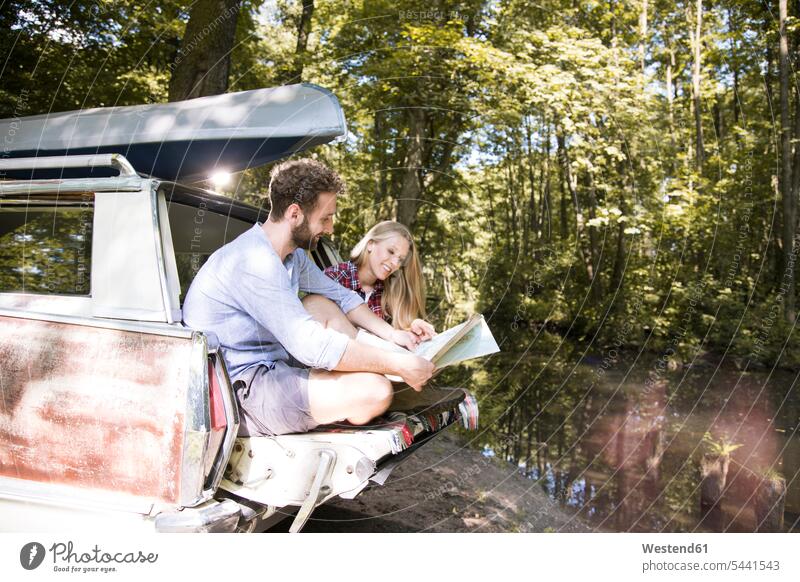 Smiling young couple with map and canoe in car at a brook maps brooks rivulet forest woods forests twosomes partnership couples automobile Auto cars motorcars