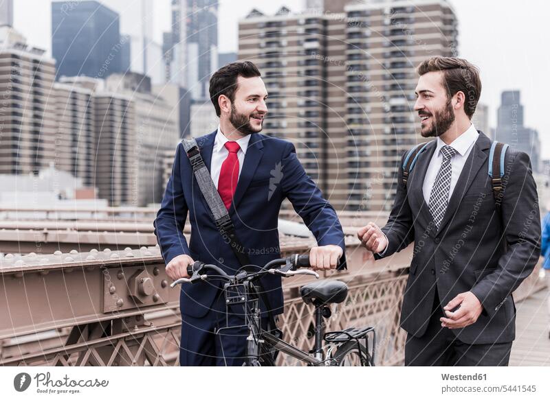 USA, New York City, two businessmen with bicycle on Brooklyn Bridge talking speaking bridge bridges smiling smile Businessman Business man Businessmen