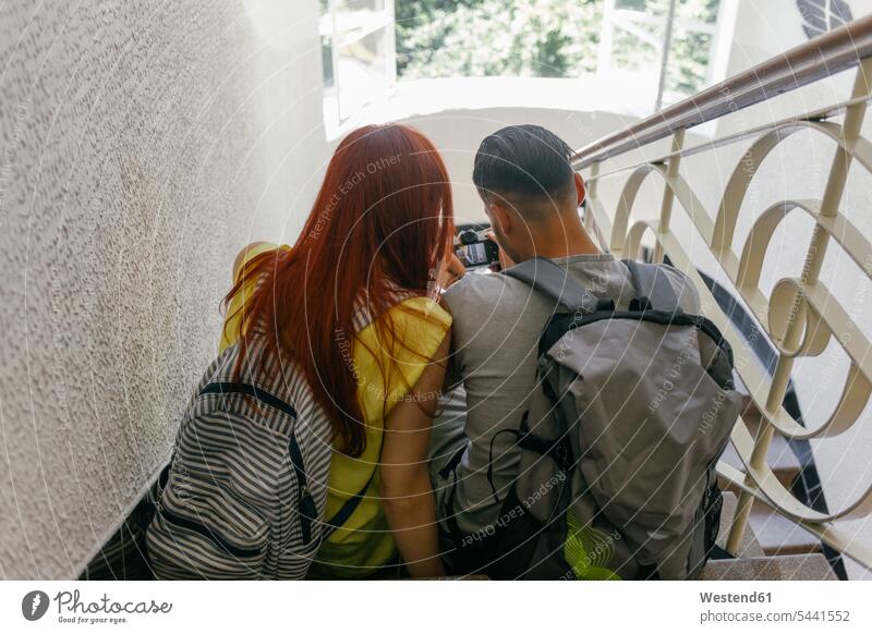 Young backpackers with camera sitting on stairs stairway couple twosomes partnership couples cameras Seated people persons human being humans human beings