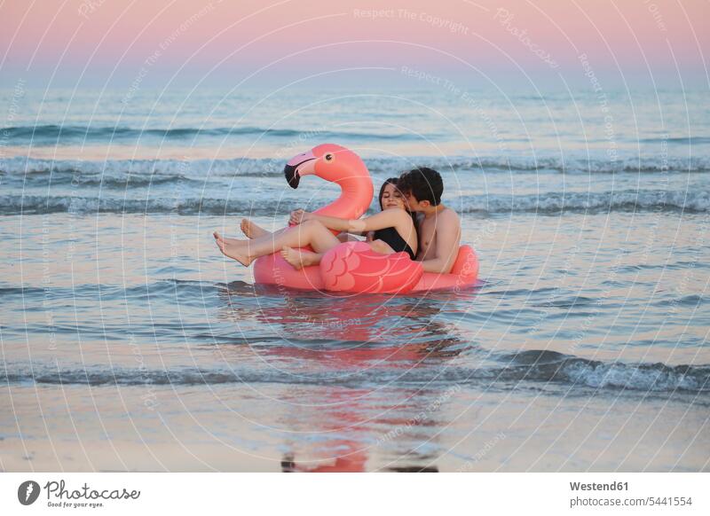 Couple in love floating with inflatable pink flamingo on the sea at sunset couple twosomes partnership couples Sea ocean people persons human being humans