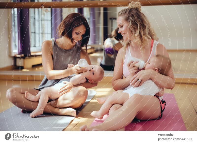 Two mothers bottle-feeding their babies in exercise room baby infants nurselings mommy ma mummy mama exercising training practising Fun having fun funny smiling