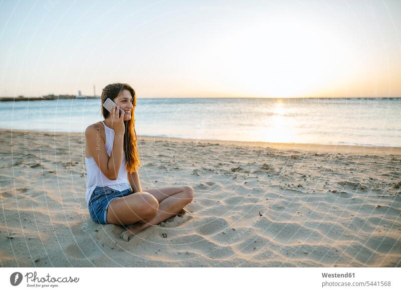 Young woman talking on cell phone on the beach at sunset mobile phone mobiles mobile phones Cellphone cell phones beaches sea ocean females women on the phone