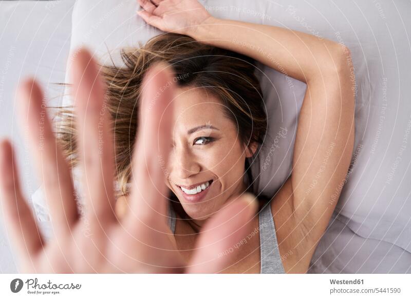 Portrait of smiling woman lying in bed raising her hand beds face faces portrait portraits human hand hands human hands laying down lie lying down females women