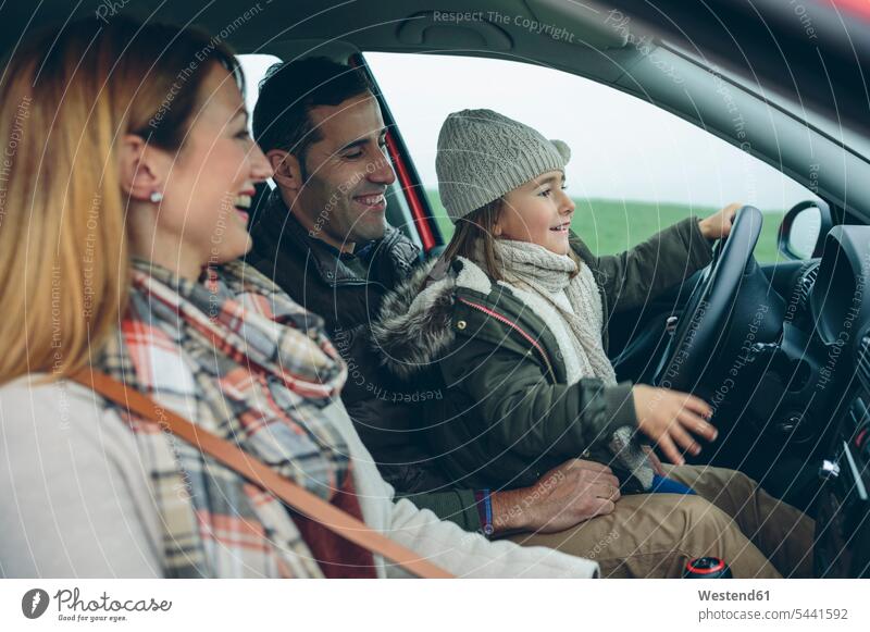 Happy family in car with little girl on father's lap pretending to drive automobile Auto cars motorcars Automobiles driving females girls smiling smile families