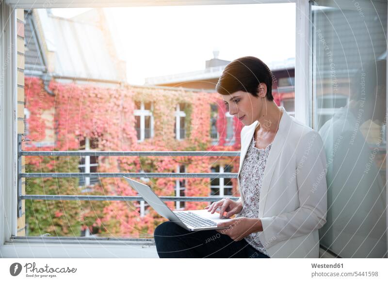 Woman using laptop at the window businesswoman businesswomen business woman business women Laptop Computers laptops notebook females working At Work